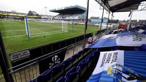 A wide shot of the Memorial Stadium, home of Bristol Rovers, showing flags on seats and the main stand