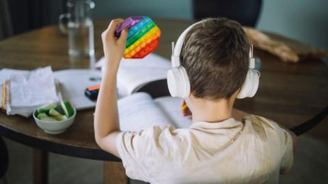 Rear view of boy listening to music and playing with push pop toy while doing homework.