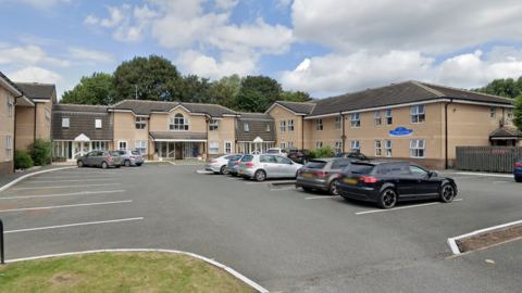 A car park with several cars in front of a large two-storey building.