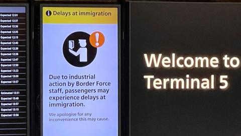 An arrivals board displays a message warning users of terminal 5 about industrial action by Border Force staff, at Heathrow Airport