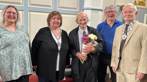 The Farmer Family standing together smiling. Robin is in the middle holding a bunch of flowers