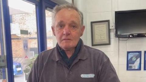 A man standing inside a shop looking just past the camera