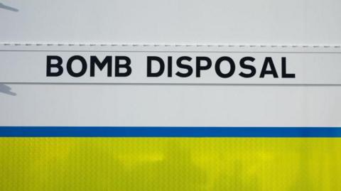 The side of a white vehicle with the words bomb disposal written on it in black, bold text. 