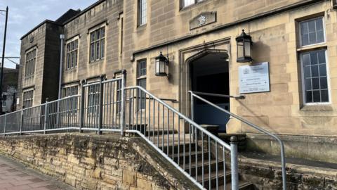 The entrance to the magistrates' court in Carlisle. Steps lead up to the arched entrance of the sandstone building, which has a sign for the magistrates' court. 