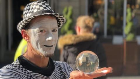 A mime artist dressed in black and white holding a glass ball. 