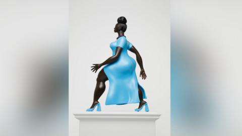 A statue of a woman of colour wearing a striking baby blue dress with matching high heels of the same colour. She has her hair up in a bun and is wearing a black beaded necklace. She is walking with purpose with one arm in front of the other.