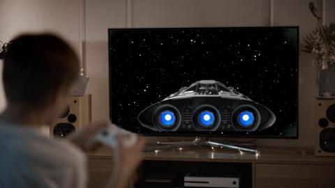 Boy playing video game with a spaceship on screen. 