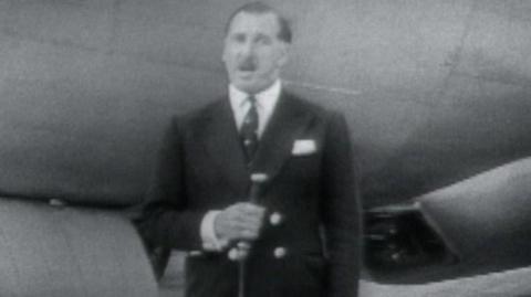 ý presenter with a microphone stands in front of a plane