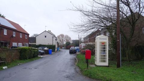 View of houses in Carr Lane in Weel with cars parked on drives and a cream phone box and red post box in the foreground