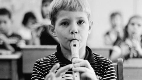 Black and white photo of a young boy playing the recorder in school