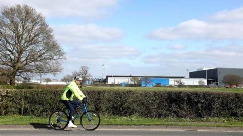 A cyclist wearing a green high-visibility jacket cycles past a sports stadium in York.