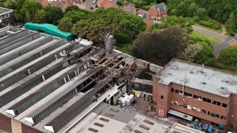A picture taken with a drone, showing part of the fire-damaged factory, with homes behind it, divided by trees.