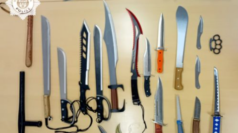 A light brown table with dozens of sharp machetes or zombie style knives