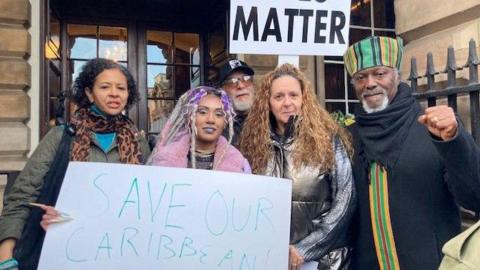 Protesters outside Liverpool Town Hall holding signs saying 'Save our Caribbean Centre' and 'Black Lives Matter'. 