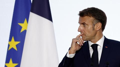 Macron in profile wears a tie and blazer next to an EU flag at a press conference at the 19th Francophonie Summit at the Grand Palais in Paris