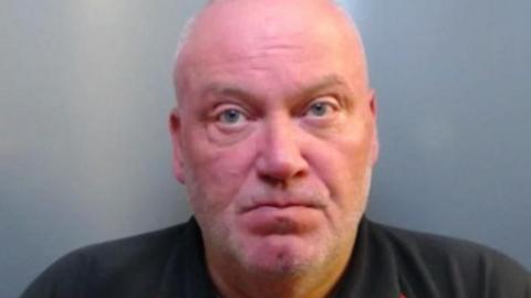 Mugshot of Ian Mcaninley. He is bald with faint grey stubble and a very red face and wearing a black polo shirt