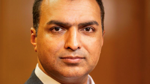 A promotional headshot image of Councillor Shahbaz Sarwar, with short hair and wearing a grey suit and white shirt.