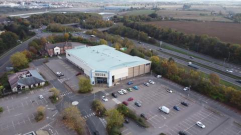 A drone shot of the area surrounding the cinema. The Odeon building, a large grey building is the largest building in the area with a largely empty car park surrounding it.