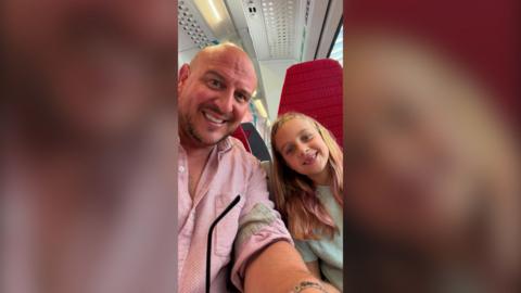 Rob and his daughter Mabel sitting on a train and smiling