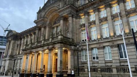 The exterior of The Council House, headquarters of Birmingham City Council. The building has two flagpoles outside of it, and comprises of a series of columns and a large archway above the entrance.