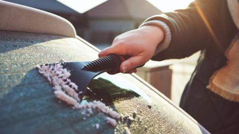 A person scraping ice off the rear windscreen of their car.