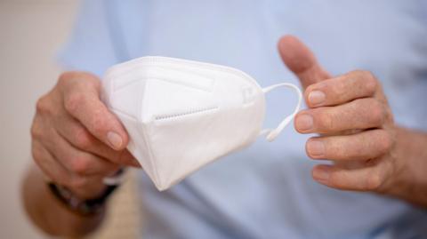 A person wearing a blue t-shirt holding a white face mask.