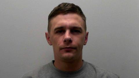 Jack Allinson has short dark hair and is clean shaven. He is wearing a grey round neck jumper.