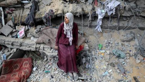 A Palestinian woman sits on the ledge of a heavily damaged building in Gaza