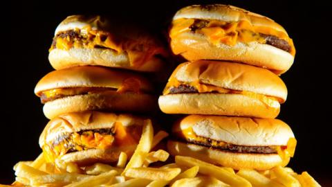 Six burgers stacked on top of a pile of chips, they and other fast foods are among those that will be affected by the new rules