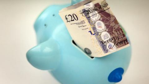 Blue piggy bank with a £20 note in it