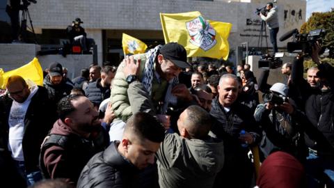 Freed Palestinian prisoner on person's shoulders leaning for hug