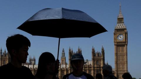 Tourists shelter from the sun underneath an umbrella, near Big Ben.