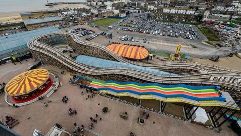 A top view of an amusement park. There are people wandering around the area. There is also a carousel and a ride.