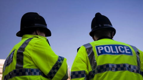 The backs of two police officers in green jackets saying 'police'.