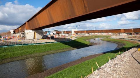 A new grass-lined river with orange metal bridges traveling over the top.