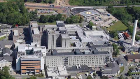 An aerial of Derriford Hospital, the helipad of the hospital is at the top right-hand side with a white cross and a yellow circle around it