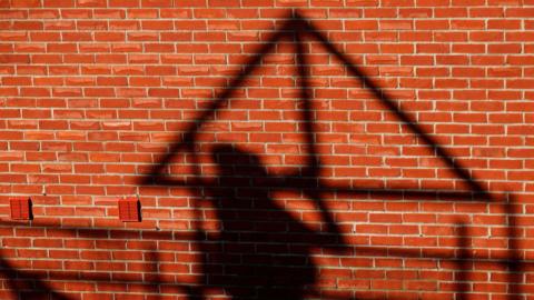 A construction worker casts a shadow carrying a wooden joist on a brick wall