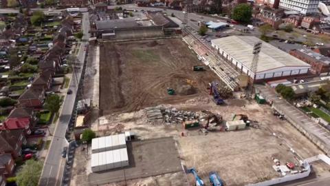 Drone photography shows old football ground being demolished, turf is all dug up and machinery present.