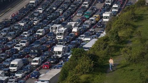 A lady walks across the cliffs while holiday and freight traffic queue to use the Port of Dover in Kent, as travellers make their way across the Channel for the summer holidays.