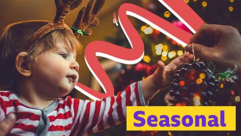 Child wearing reindeer antlers and dressing a Christmas tree. 