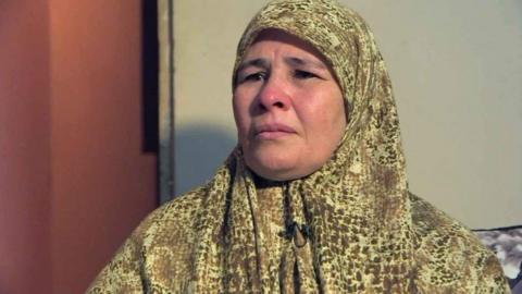 A woman wearing a headscarf looks slight off camera, clearly in emotional distress, during a ý interview