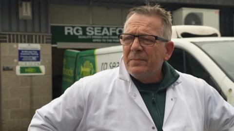 Rob Goodacre wearing a white lab coat and green jumper looks to the left of the camera