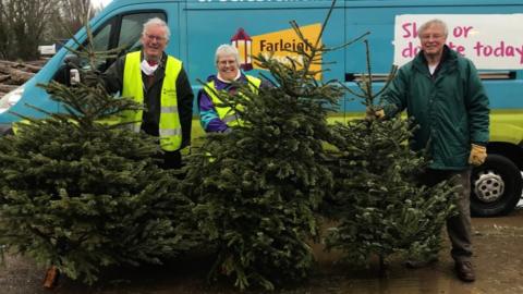 Farleigh Hospice staff standing in front of a van along with some of the donated Christmas trees.