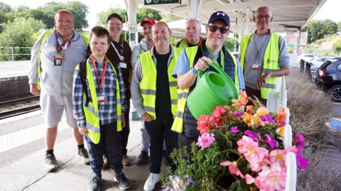 Members of The Aldingbourne Trust water a plant at a railway station