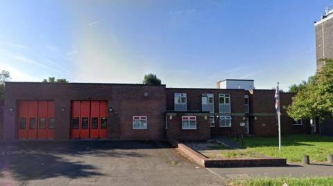 A street view image of the fire station, a red brick, two-storey building. On the left two sets of tall, red garage doors allow access for appliances.