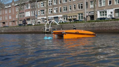 An orange floating robot gathers plastic waste in an urban waterway