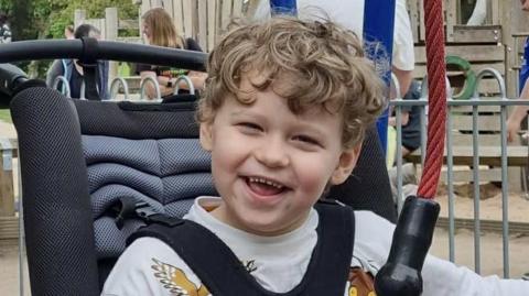 Rupert in a wheelchair on an accessible roundabout 