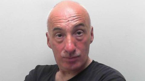 A man with folded arms stares into the camera in a police custody image