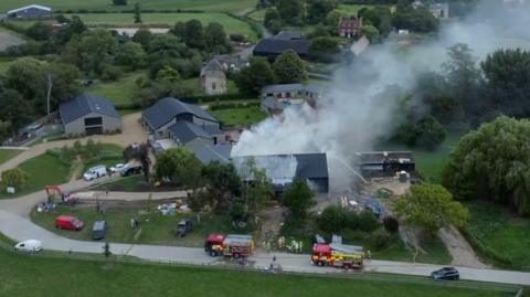 Drone video shows smoke rising high into the air as water is pumped on to the site.