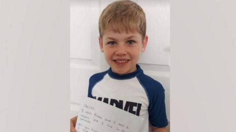 Blake with his letter. He has blond hair and is smiling.